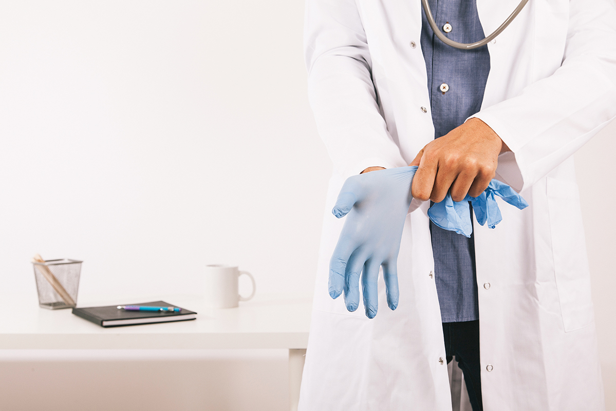 Ginekolog se sprema na pregled ili na intervenciju kod pacijentkinje, pa stavlja hirurške rukavice na ruke. Obučen je u beli mantil.
