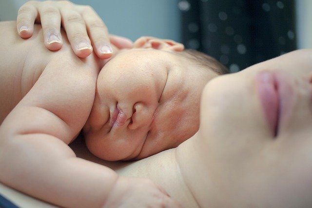 Novorođenče leži u maminom naručju i spava. 