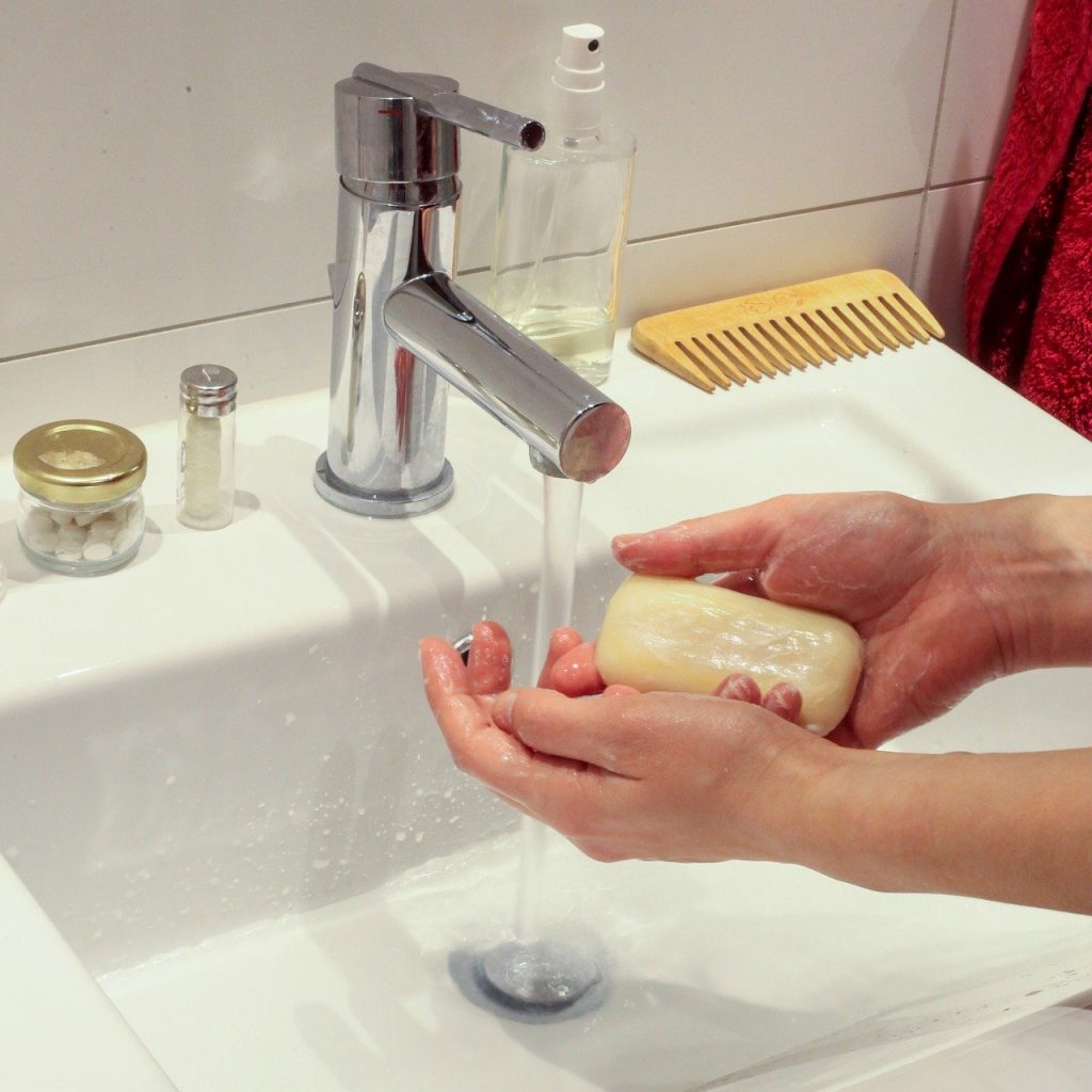 Žena pere ruke sapunom, nad lavaboom, u toaletu. Voda teče iz slavine.